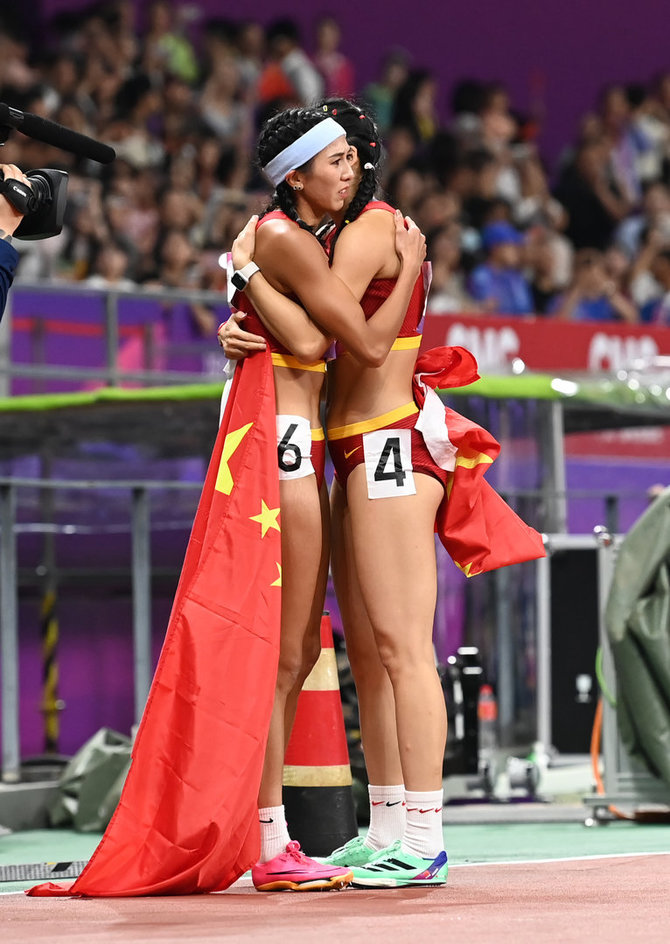 ZUMAPRESS / Scanpix nuotr./Kinijos bėgikės Lin Yuwei ir Wu Yanni pasveikino viena kitą po finišo Azijos žaidynėse. Tačiau ši jų nuotrauka cenzūruota Kinijoje dėl numerių kombinacijos.