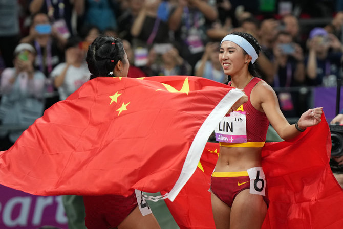 ZUMAPRESS / Scanpix nuotr./Kinijos bėgikės Lin Yuwei ir Wu Yanni pasveikino viena kitą po finišo Azijos žaidynėse. Tačiau ši jų nuotrauka cenzūruota Kinijoje dėl numerių kombinacijos.