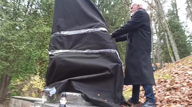 Stop kadras/Kazimieras Juraitis plėšia juodą audeklą nuo sovietinės skulptūros Antakalnio kapinėse