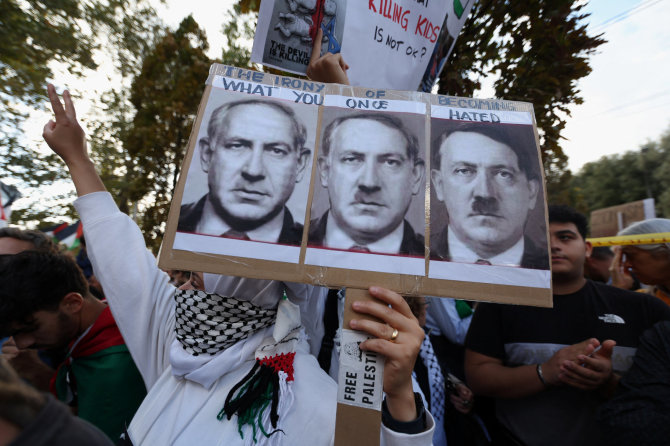 „Reuters“/„Scanpix“ nuotr./Propalestinietė protestuotoja laiko Benjamino Netanyahu portretą, kuris palaipsniui tampa Adolfu Hitleriu