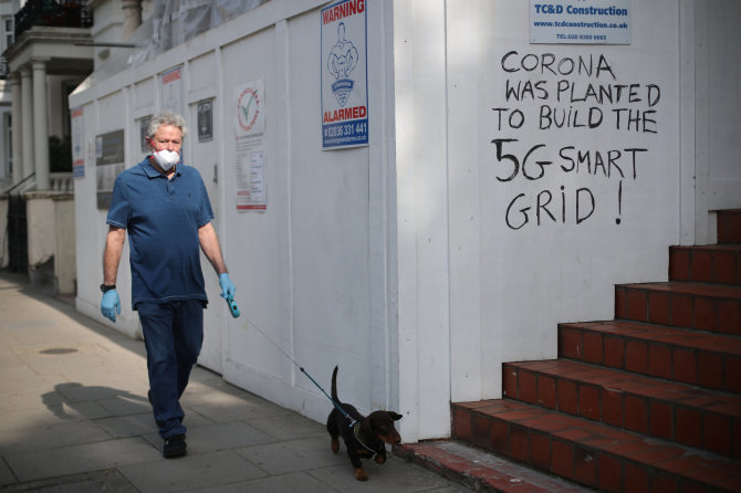 „Reuters“/„Scanpix“ nuotr./Vyras Londone greta sienos su užrašu skelbiančiu, esą COVID-19 pandemija buvo pradėta 5G ryšio tinklui išplėsti