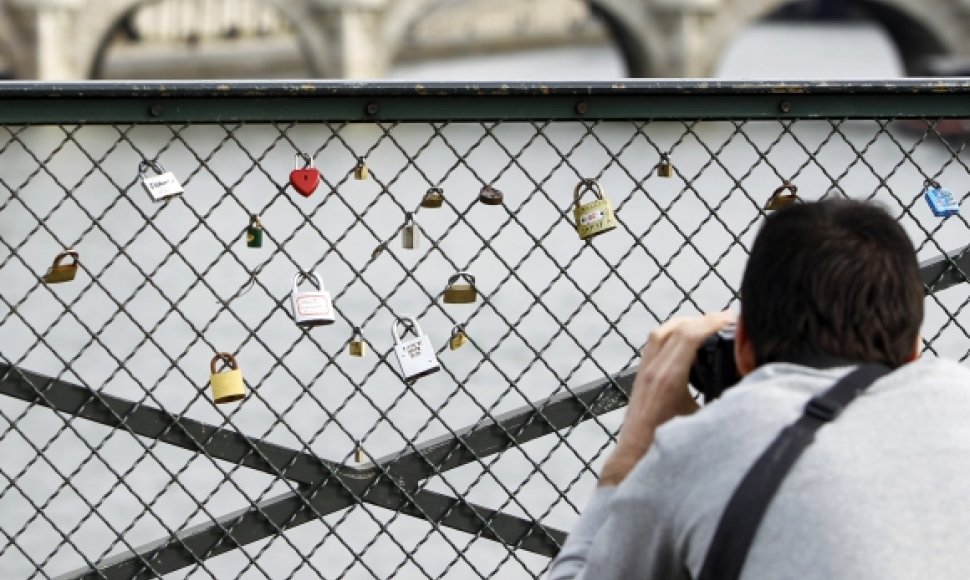 Turistas fotografuoja spynas ant Pont des Arts tilto turėklų.