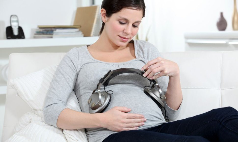 Nėščia moteris uždėjusi ausines ant pilvo