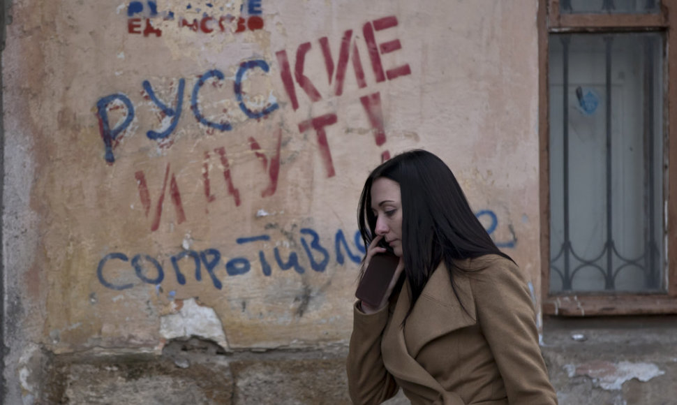 FILE - In this Friday, March 7, 2014 file photo, a woman passes by a graffiti that reads "The Russians are coming - Resistance" in Simferopol, Ukraine. For the ethnic Ukrainians and Tatars who are the minority in the strategic peninsula, it is fear that dominates days before Crimea votes in a refere