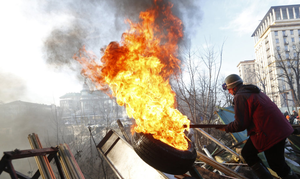 An anti-government protester moves a burning tyre at a barricade in Kiev February 21, 2014. Violence flared again in Kiev on Friday as Ukraine's opposition politicians pondered a draft deal with Russian-backed President Viktor Yanukovich which EU foreign ministers brokered to resolve the country's p