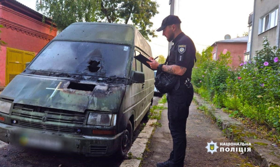 Ukrainos policijos pareigūnas apžiūrinėja per padegimą apgadintą automobilį.