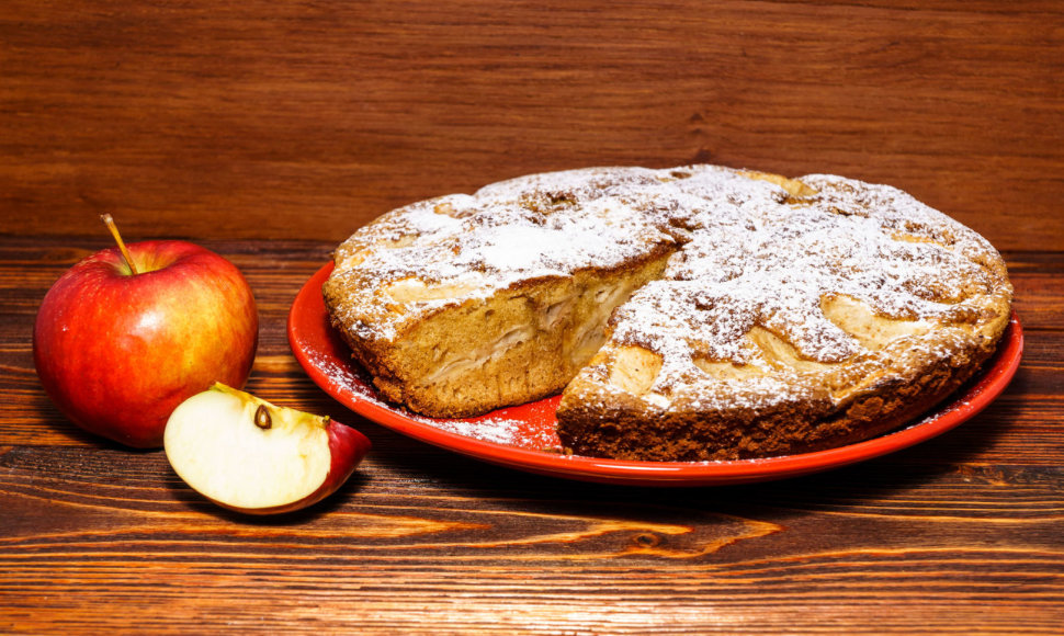 Apples and freshly baked apple pie on a rustic background of dark wood.