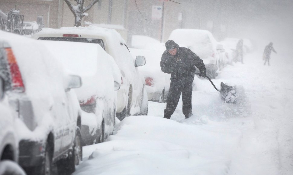Čikagoje vyras prie savo automobilio kasa sniegą.