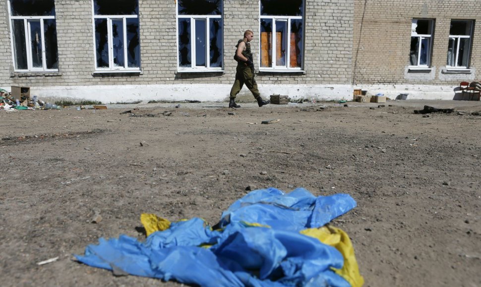 Prorusiškas teroristas eina netoli ant žemės gulinčios Ukrainos vėliavos