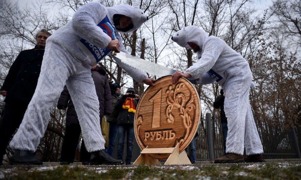 Baltaisiais lokiais apsirengę vyrai pjauna per pusę medinę rublio monetą