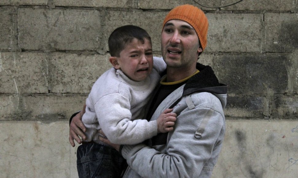 Vyras su vaiku bėga slėptis per oro reidą Alepo mieste.