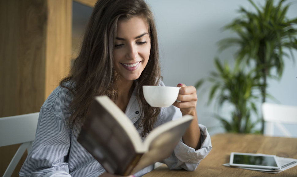 Mergina geria kavą ir skaito knygą