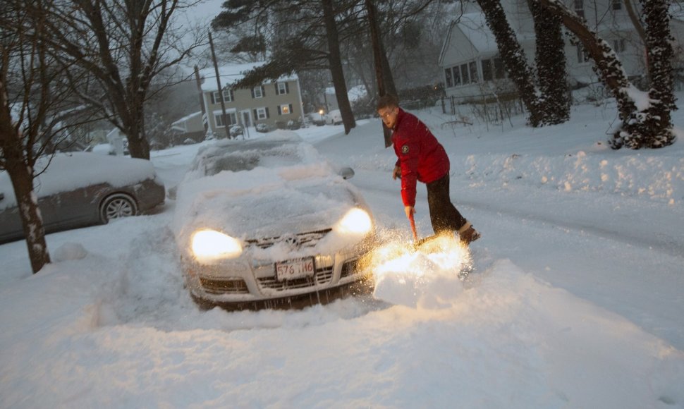 Vyras valo sniegą aplink savo automobilį.