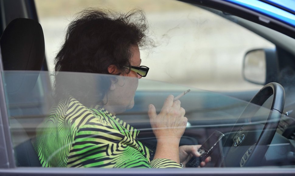 Moteris rūko automobilyje ir naudojasi mobiliuoju telefonu