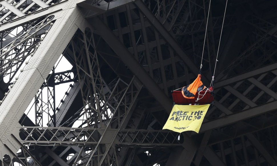 „Greenpeace“ atstovas protestuoja palapinėje, kabančioje ant Eiffelio bokšto sijos.