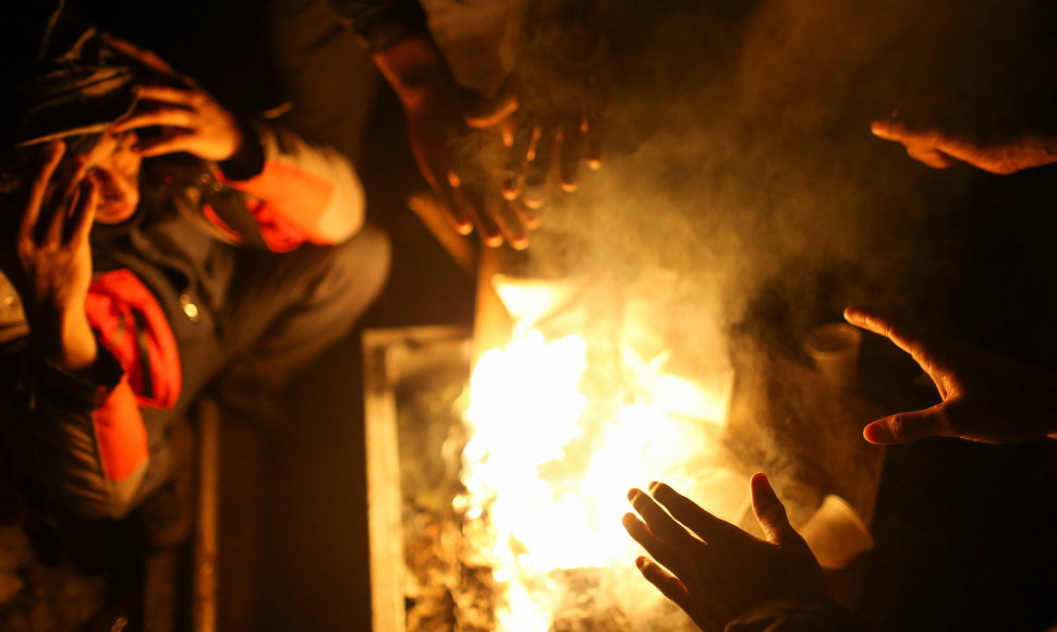 Migrantai šildosi prie atviros ugnies.