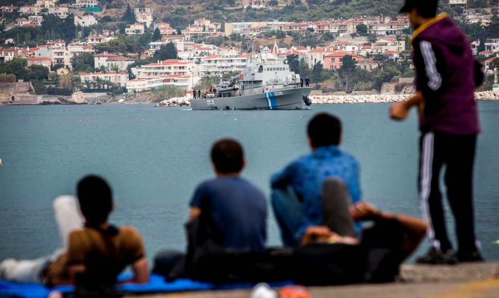 Migrantai stebi, kaip į Lesbo salos uostą karinis laivas atplukdo išgelbėtus jų likimo brolius.