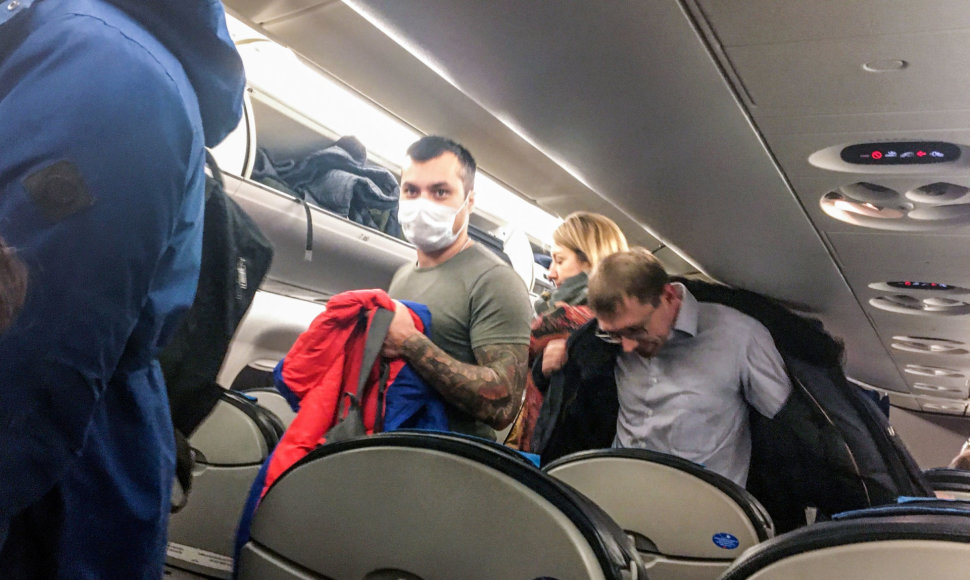 Žmonės lėktuve su apsauginėmis kaukėmis