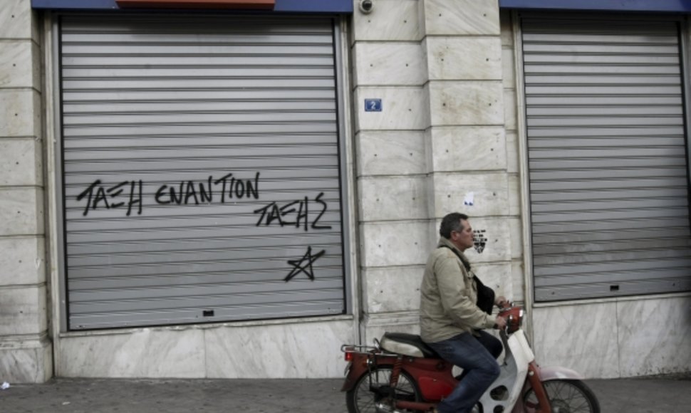 Žmogus važiuoja pro uždarytą banko skyrių Atėnuose.