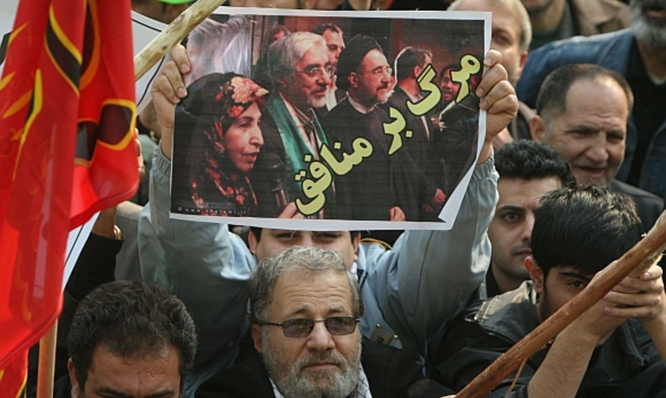 Vyriausybės šalininkas laiko plakatą, kuriame pavaizduoti buvęs šalies prezidentas Mohammadas Khatamis ir Miras Hosseinas Mousavis su žmona. Užrašas ant plakato skelbia: „Mirtis veidmaniams“.