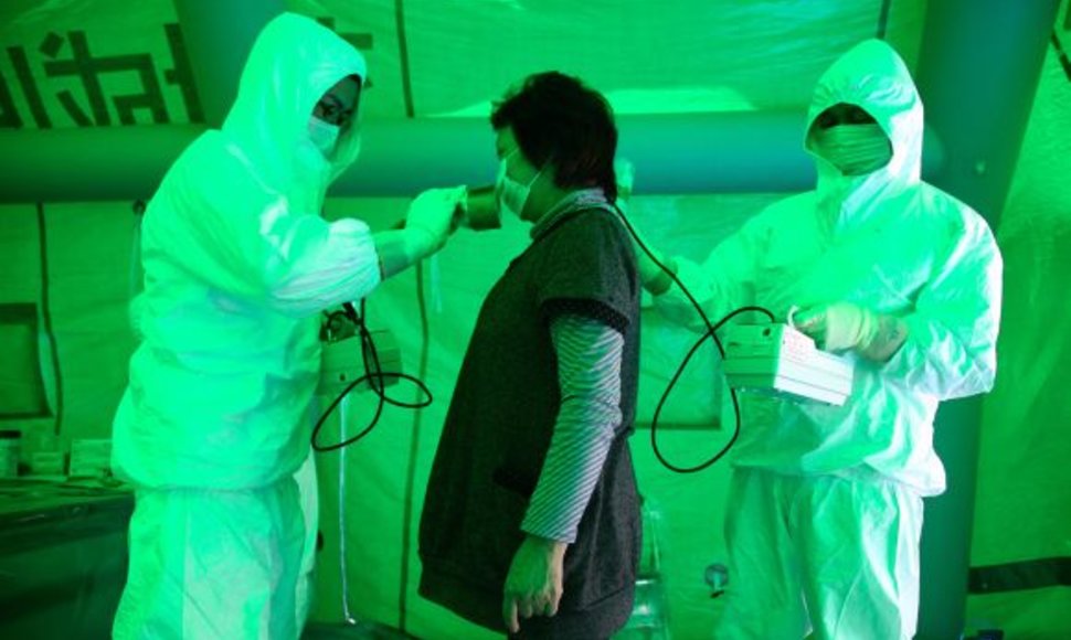 Japonijos medikai radiacijos matuokliais tikrina evakuotą moterį.