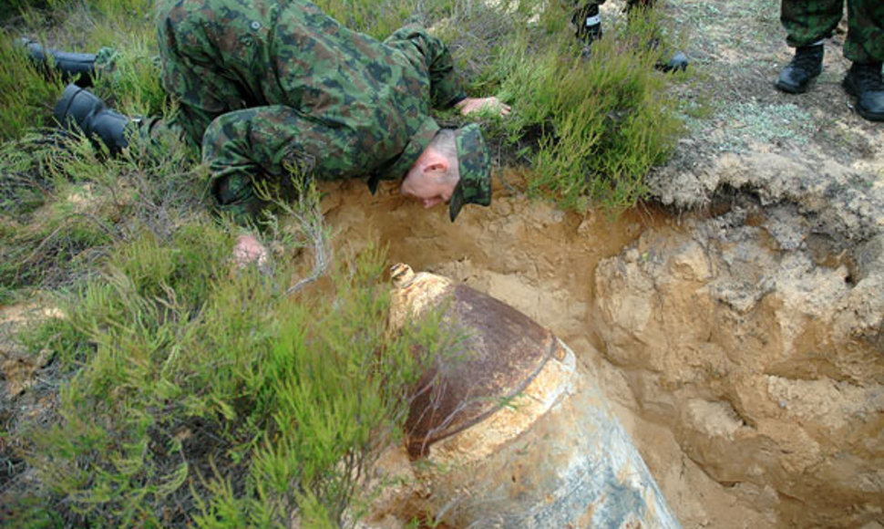 Išminuotojas buvusiame Rūdninkų poligone apžiūri rastą bombą. Sprogmenų Rūdninkuose randama nuolat.