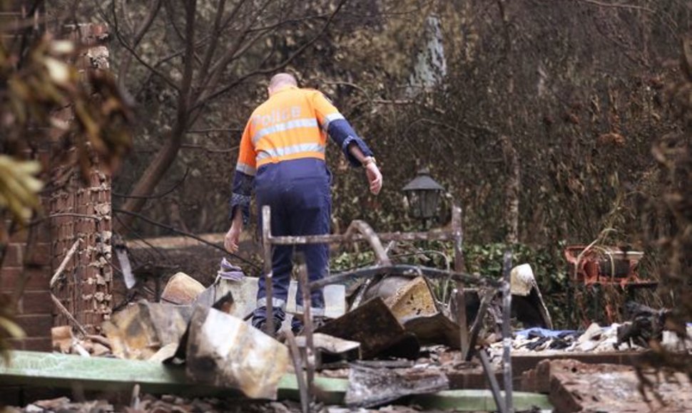 Policijos pareigūnas apžiūrinėja vietą, kur sudegė namas. Jame žuvo penki žmonės.