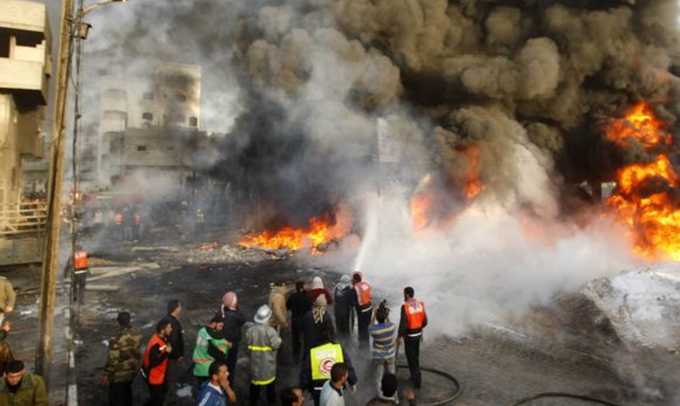 Po Izraelio atakų Palestinos ugniagesiai mėgina užgesinti liepsnojančius pastatus ir gatves.