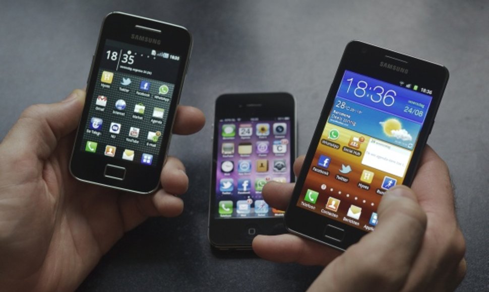 Vyras rankose laiko „Samsung Galaxy S II“ (d.) ir „Galaxy Ace“ išmaniuosius telefonus. Fone – „Apple“ telefonas „iPhone 4“.