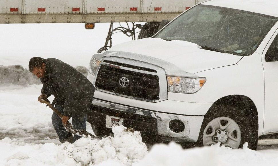 Vyras atkasinėja sniege užklimpusį automobilį.