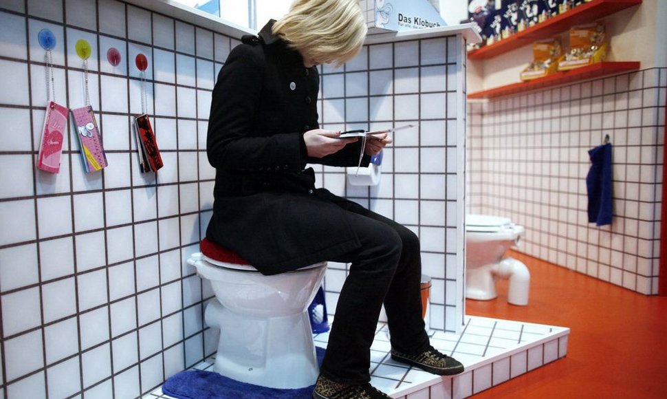 Parodoje moteris skaito lankstinunką sėdėdama ant tualeto