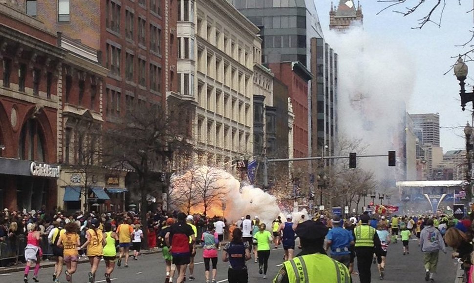 Bostono maratono dalyviai bėga link finišo, kairėje pusėje matomas prasidėjęs sprogimas.