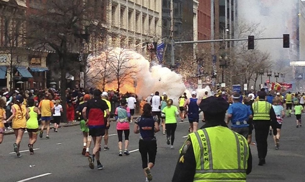 Bostono maratono dalyviai bėga link finišo, kairėje pusėje matomas prasidėjęs sprogimas.