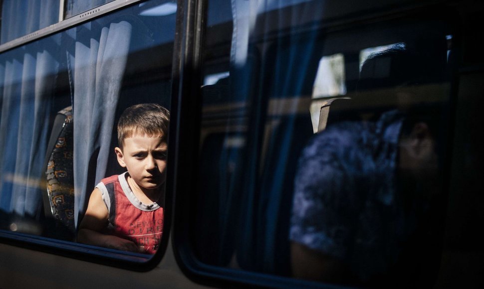 Iš Rytų Ukrainos išvažiuojantis berniukas žiūri per autobuso langą.