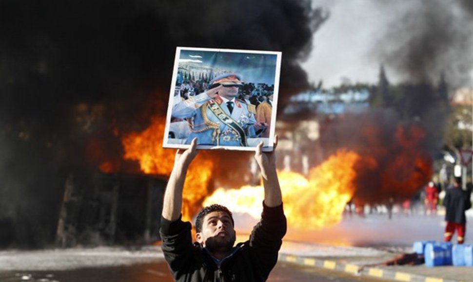 Protestuotojai laiko Muamaro Kadhafi portretą netoli degančio benzinvežio.