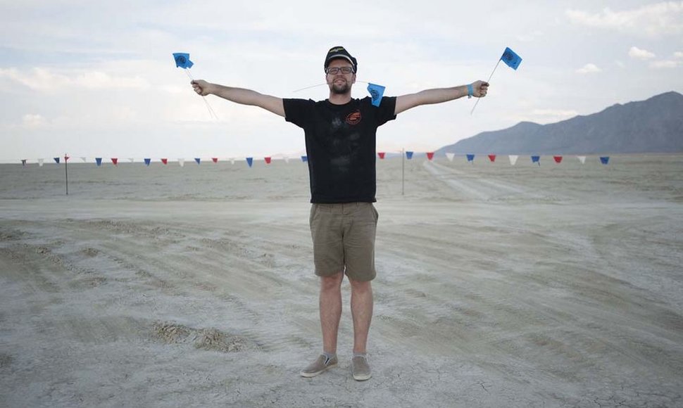 Pirmąkart į „Burning Man“ atkeliavęs Vytautas pozuoja su stovyklos ribas žyminčiomis vėliavėlėmis