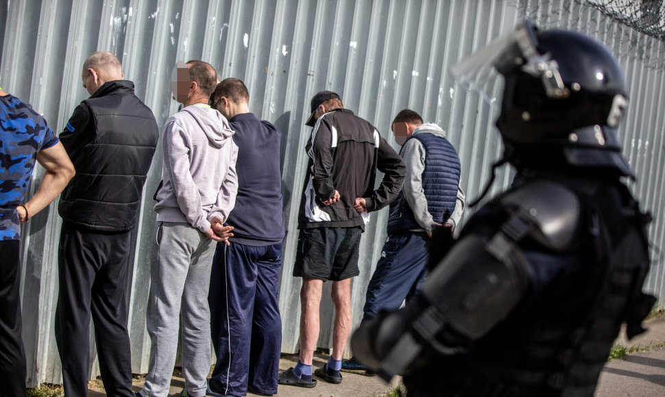 Grupė nuteistųjų stovi prie sienos saugomi Kalėjimų departamento pareigūno
