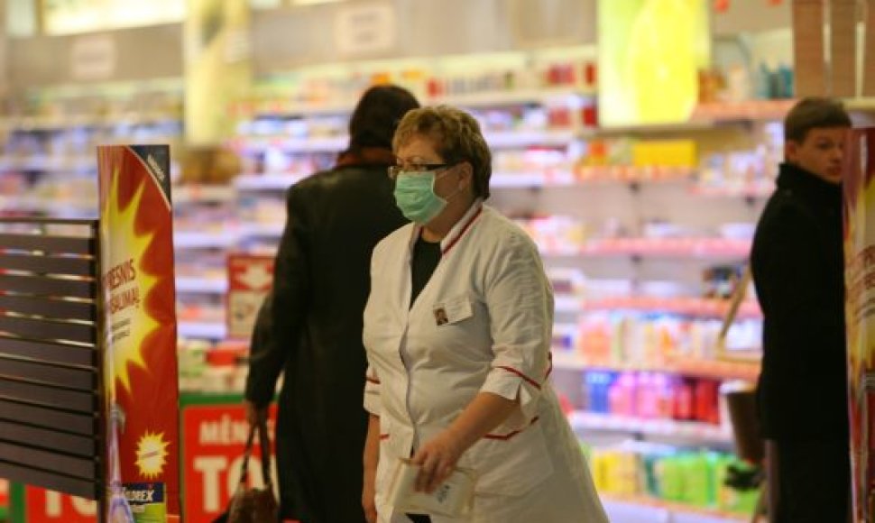 Vaistinės darbuotoja nuo siautėjančio gripo saugosi dėvėdama kaukę.