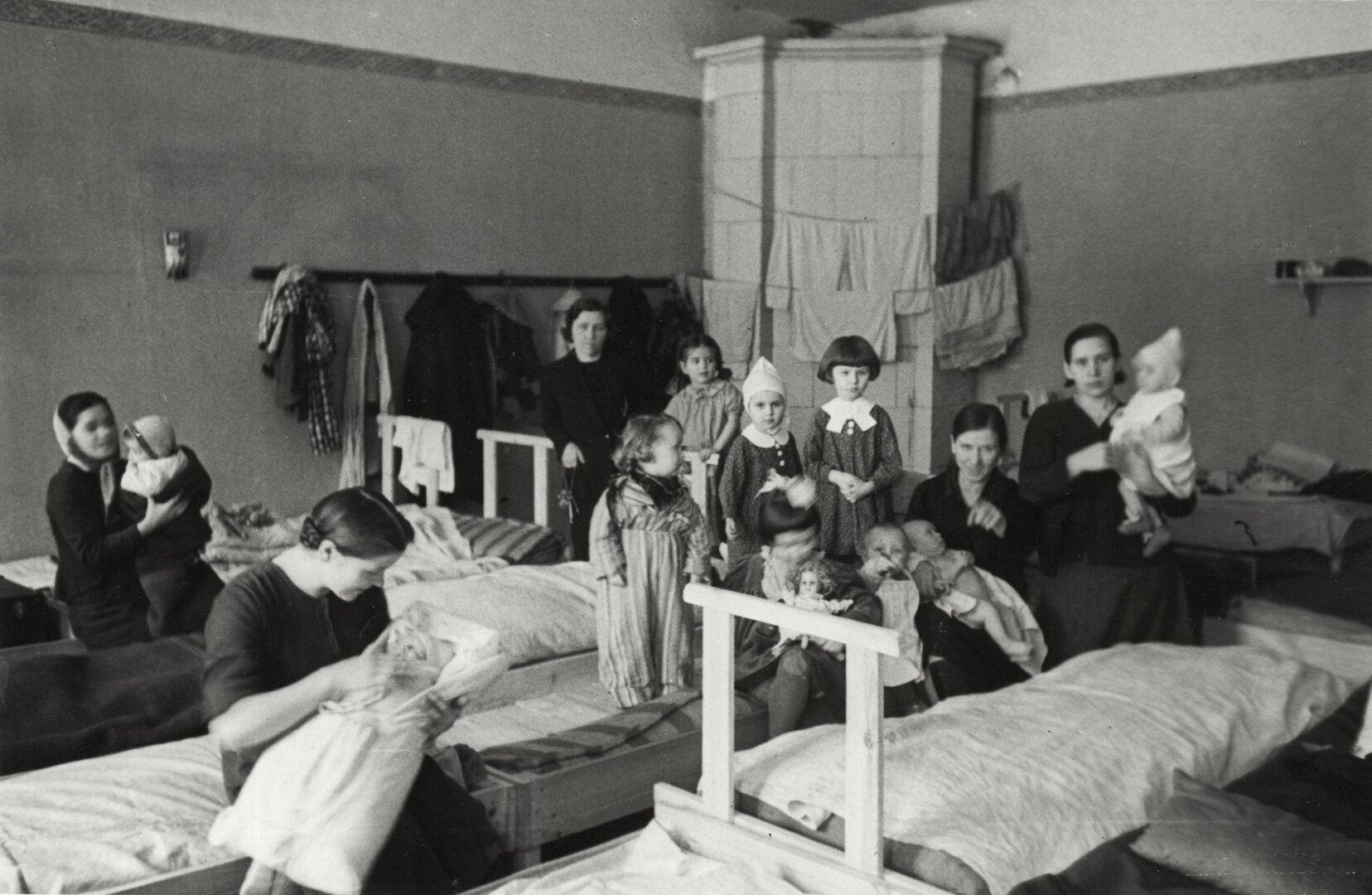 Mažų vaikučių Vilniuje, kuriems dar reikalinga motinų globa ir priežiūra, miegamasis. Keturios jaunos motinos su kūdikiais, o penktoji mažytė mergiotė su lėle, kurią ji taip pat sups &ndash; kaip ir suaugusios motinos...